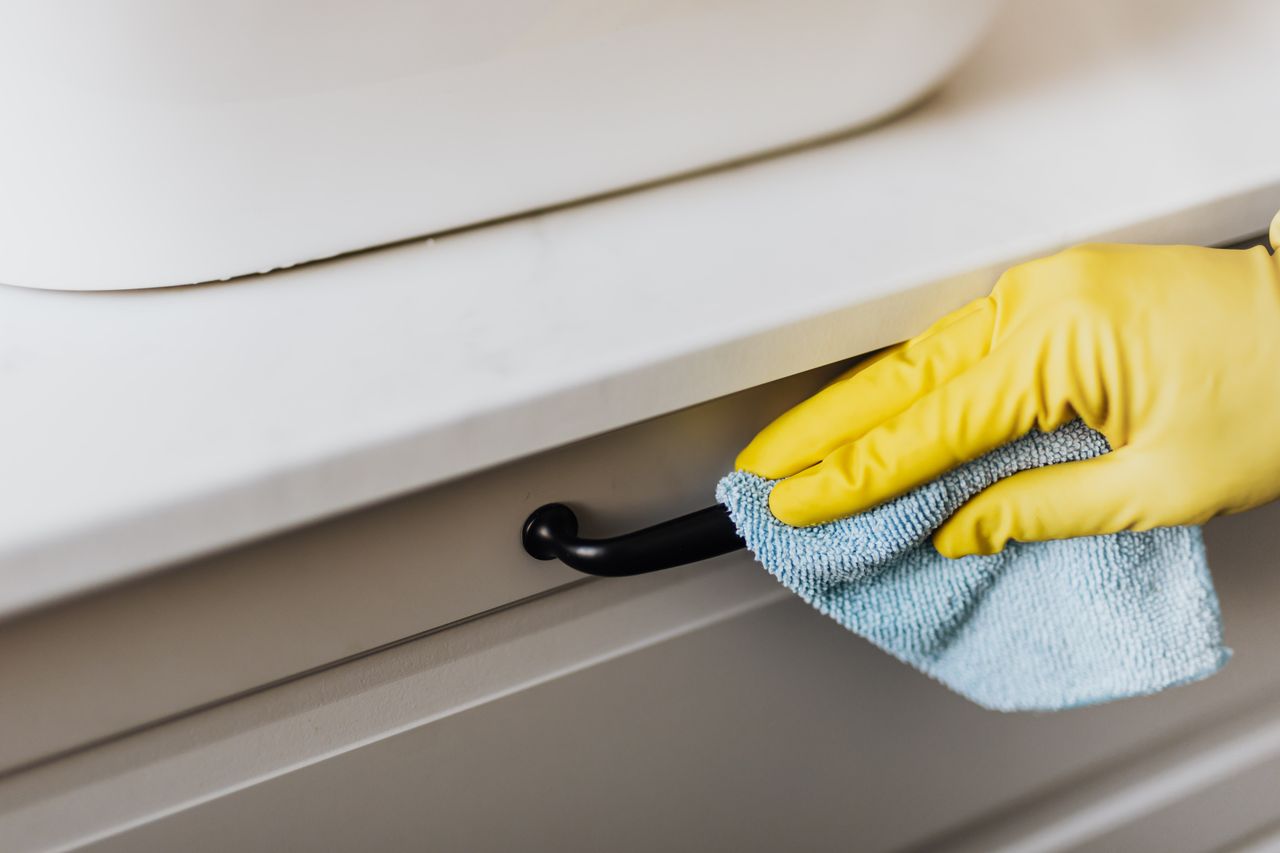 about-04 From above of crop faceless person in yellow gloves cleaning handle of cabinet with microfiber cloth in modern bright bathroom