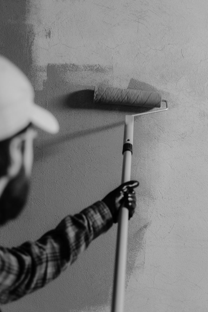 why-choose-us-02 Black and white image of a painter using a roller on an interior wall.